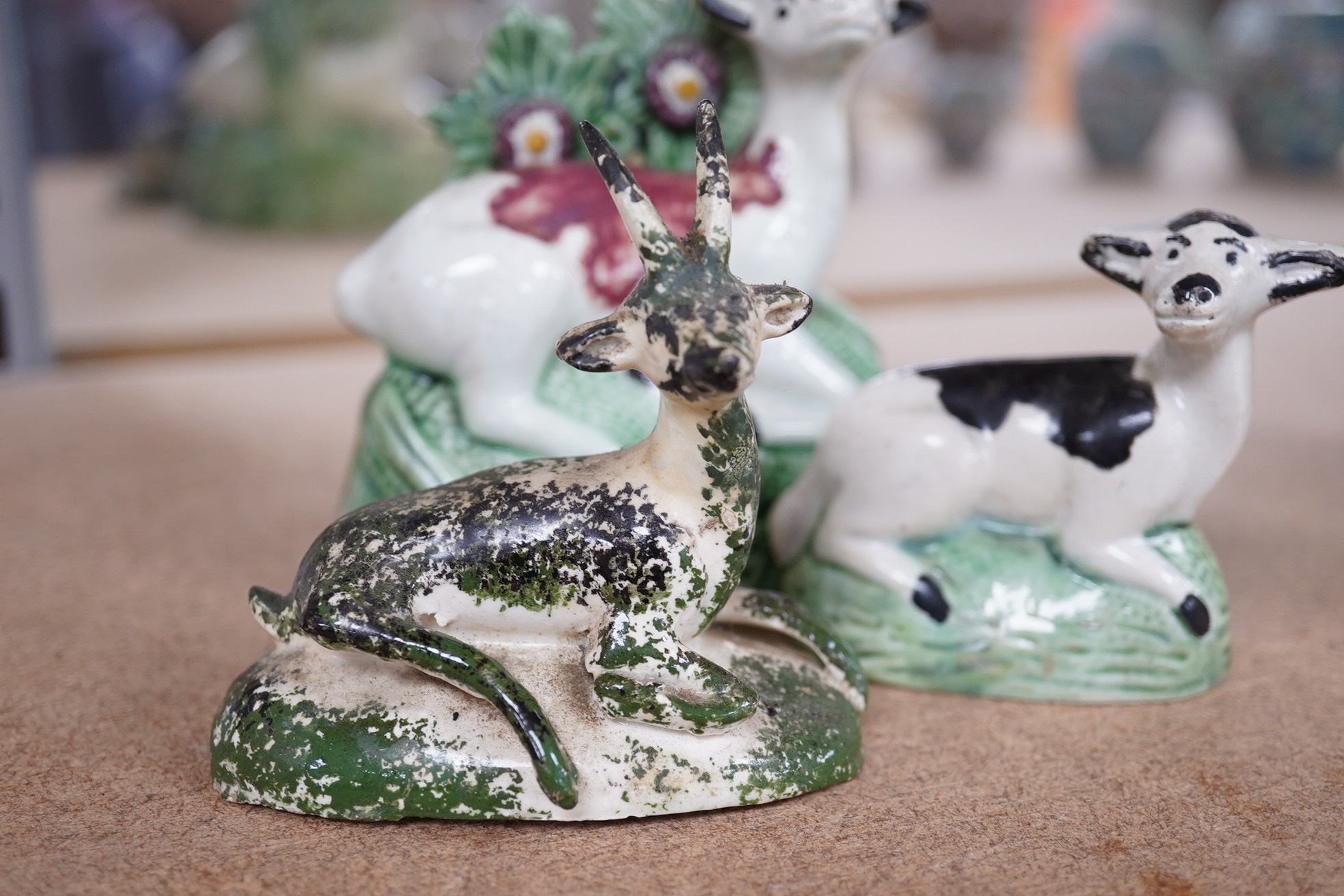 Two late 18th century Staffordshire coloured creamware figures of recumbent cows and a spongeware deer, largest 10cm wide (3). Condition - restored